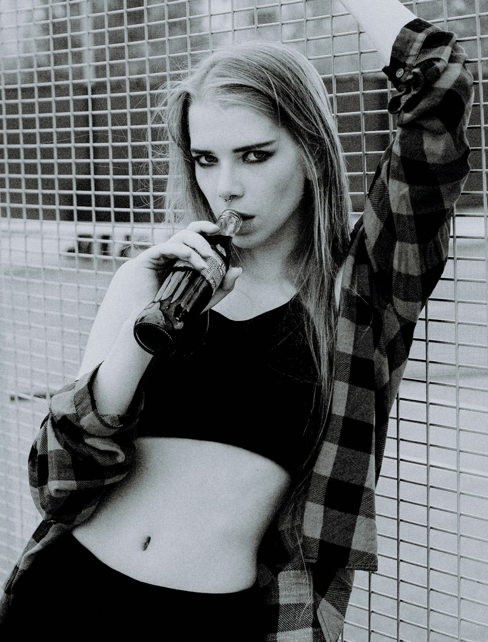 a woman drinking a drink while standing in front of a fence