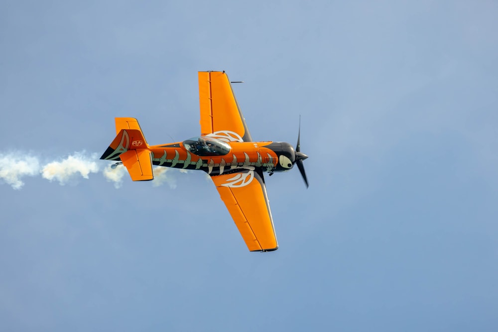 a small orange airplane flying through a blue sky