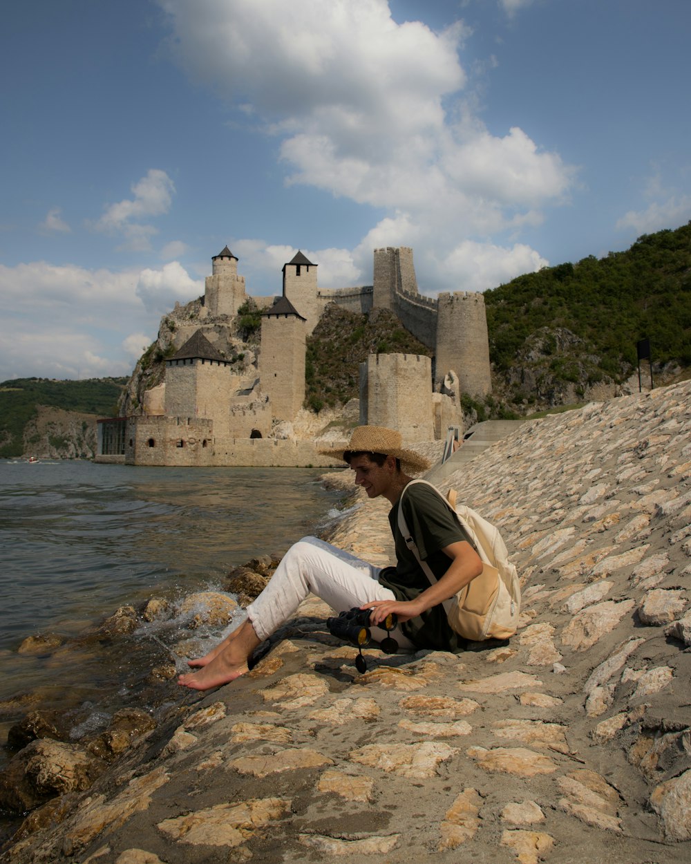 a man sitting on a rock next to a body of water