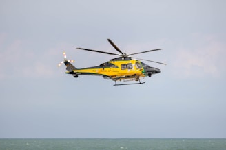 a yellow and black helicopter flying over the ocean