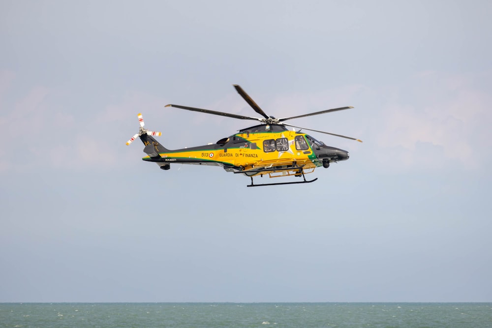 a yellow and black helicopter flying over the ocean