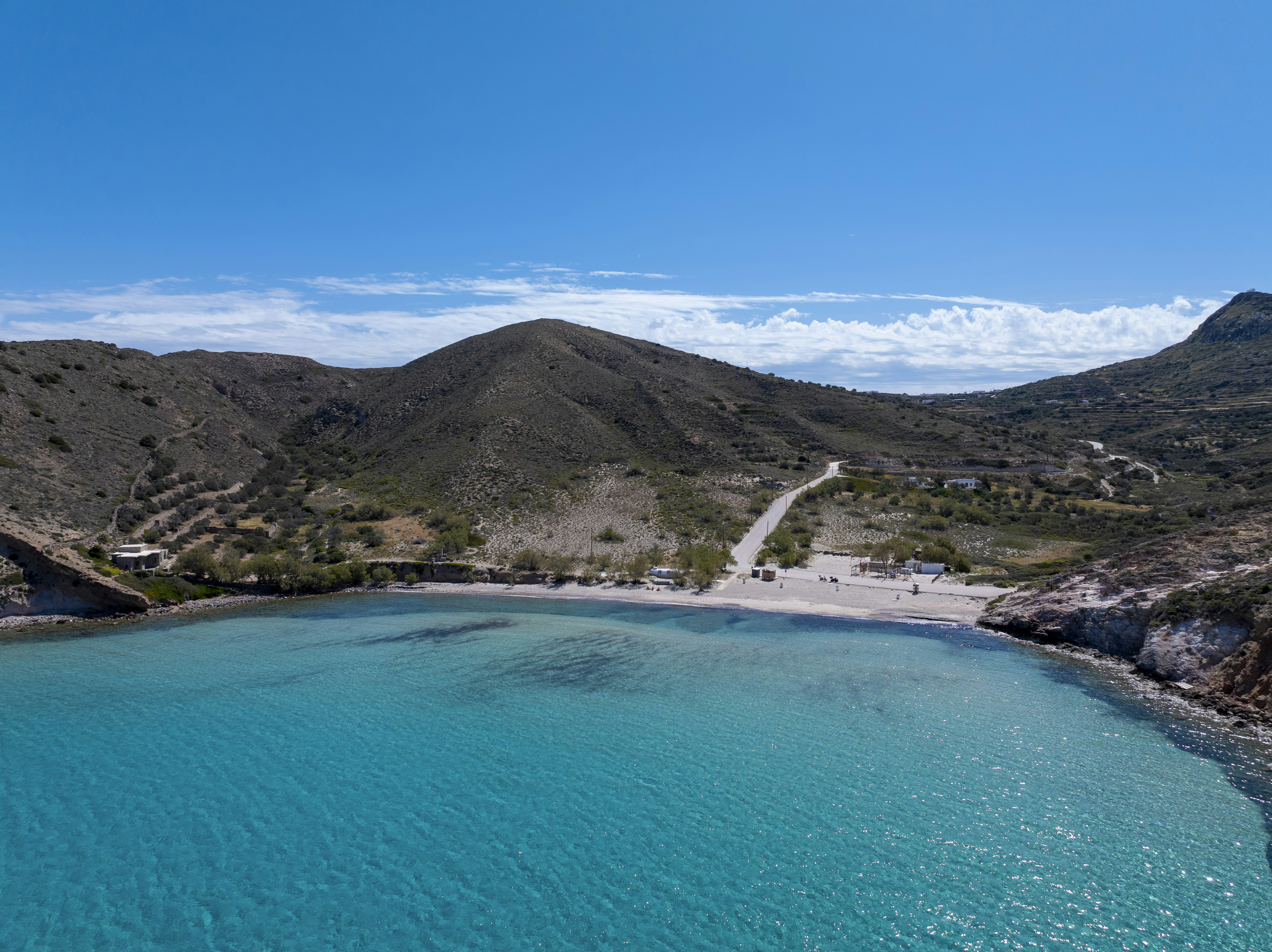 a blue body of water surrounded by mountains, Plathiena Beach, a typical beautiful beach of Greek Summer located in MIlos.