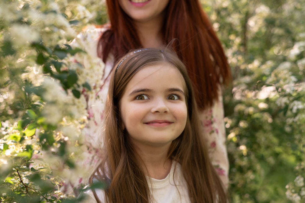 a woman standing next to a little girl in a forest