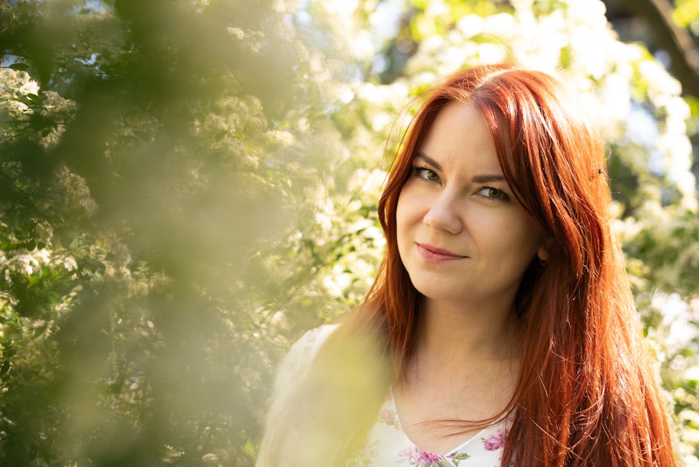 a woman with red hair standing in front of trees