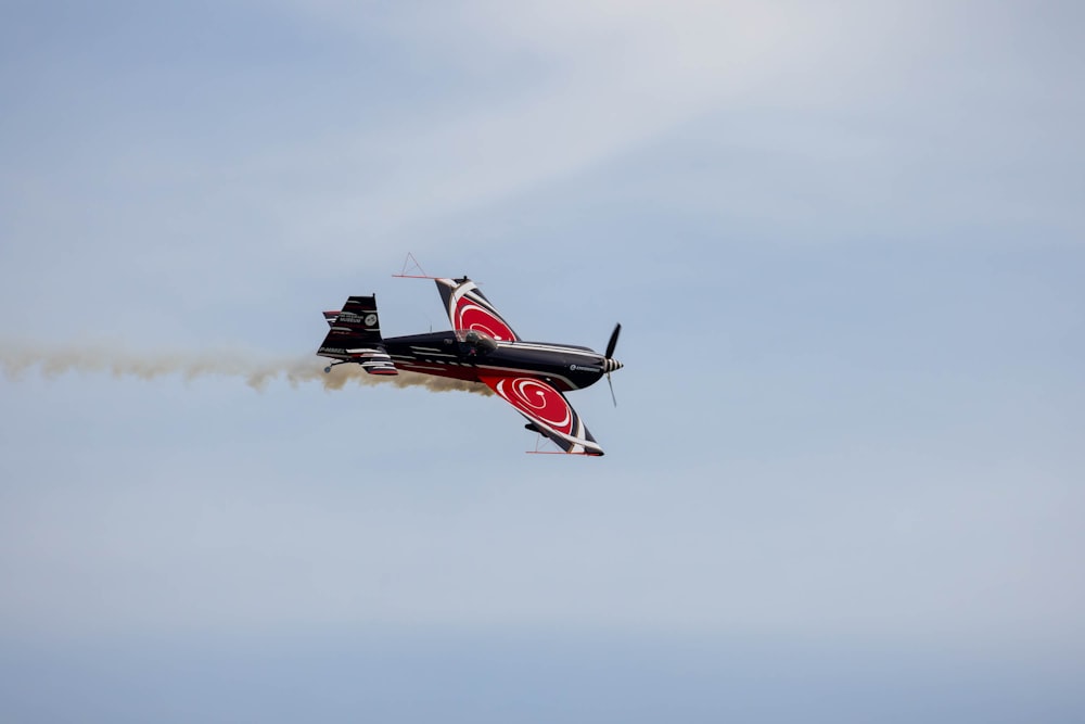 a red and black plane flying through a blue sky