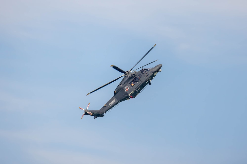 a military helicopter flying through a blue sky