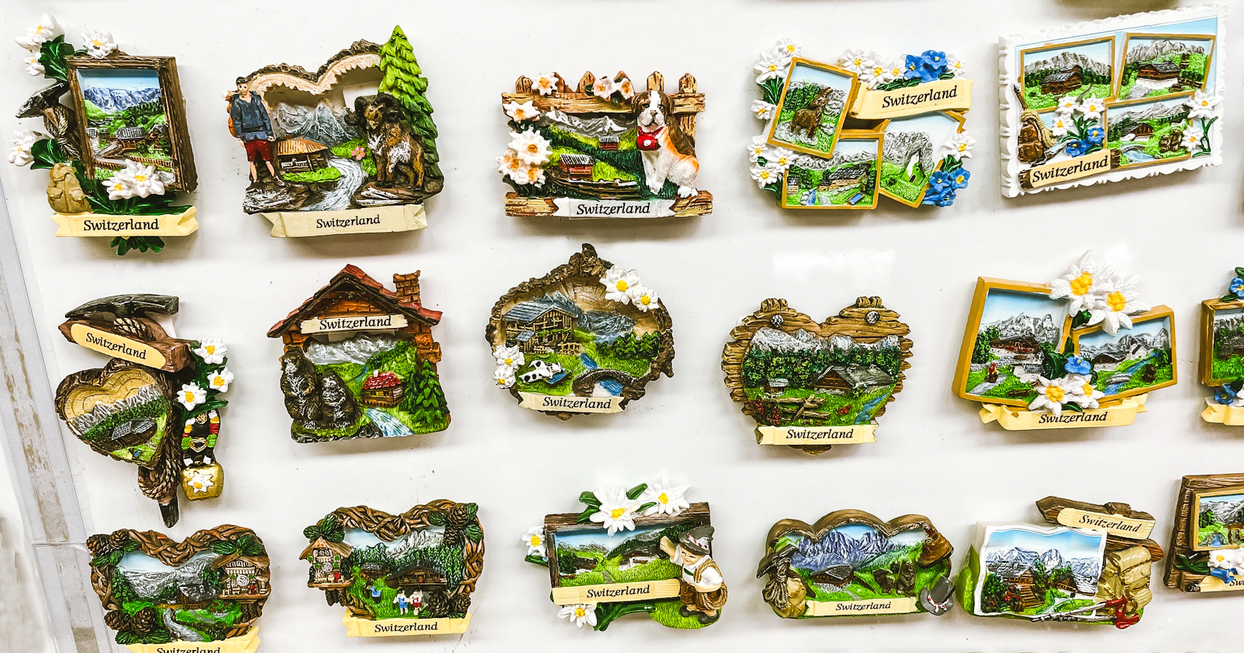 Rows of molded souvenir magnets showing chalets, mountains and white flowers on a white shop display board
