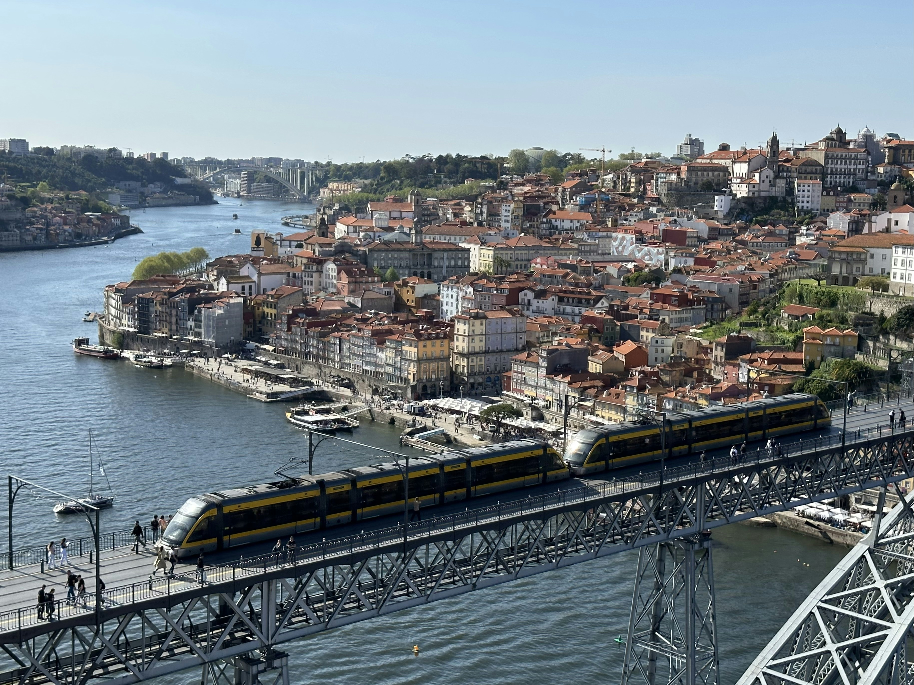 a train traveling over a bridge over a river, A Porto Metro tram is going over the Dom Luís I Bridge with the view of the Ribeira, Vila Nova de Gaia, Porto, Portugal, April 2023