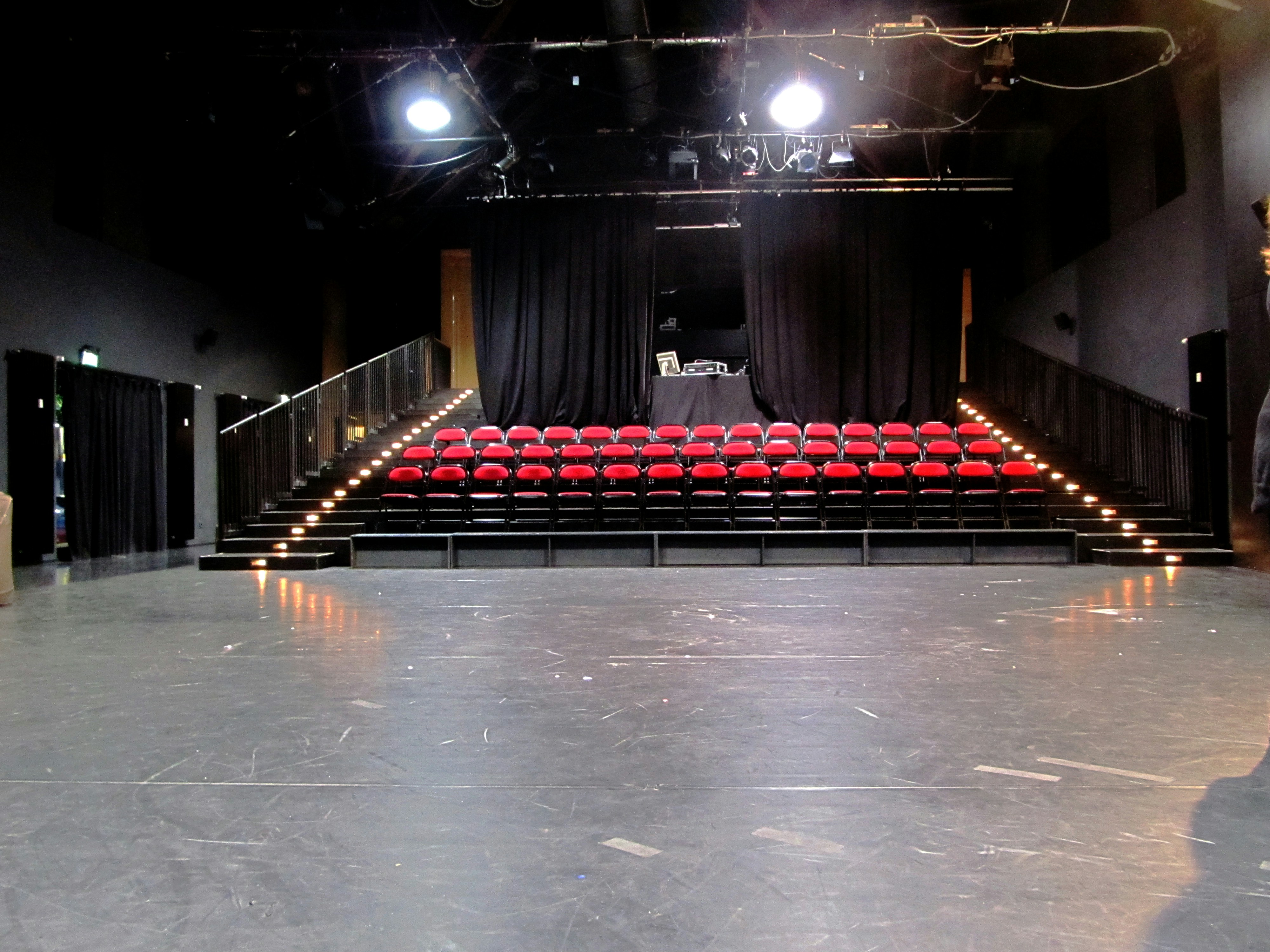 Theater stage with red velvet curtain under spotlight, dark auditorium seats in background