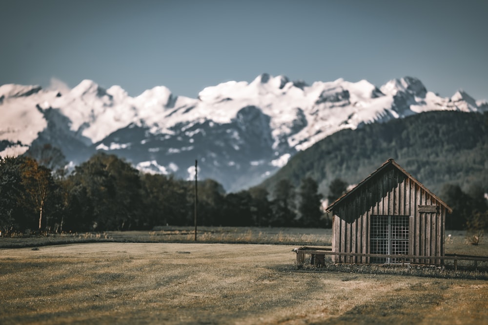 a small cabin in the middle of a field with mountains in the background