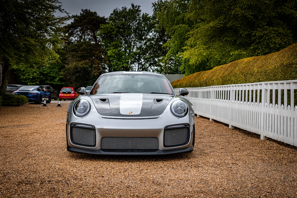 a silver sports car parked in front of a white fence