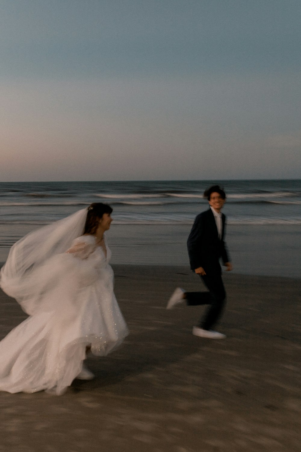 a bride and groom running on the beach