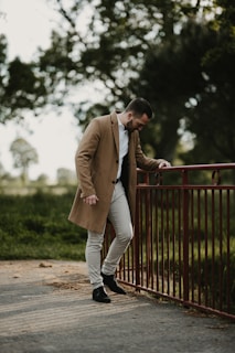 a man leaning against a fence wearing a coat
