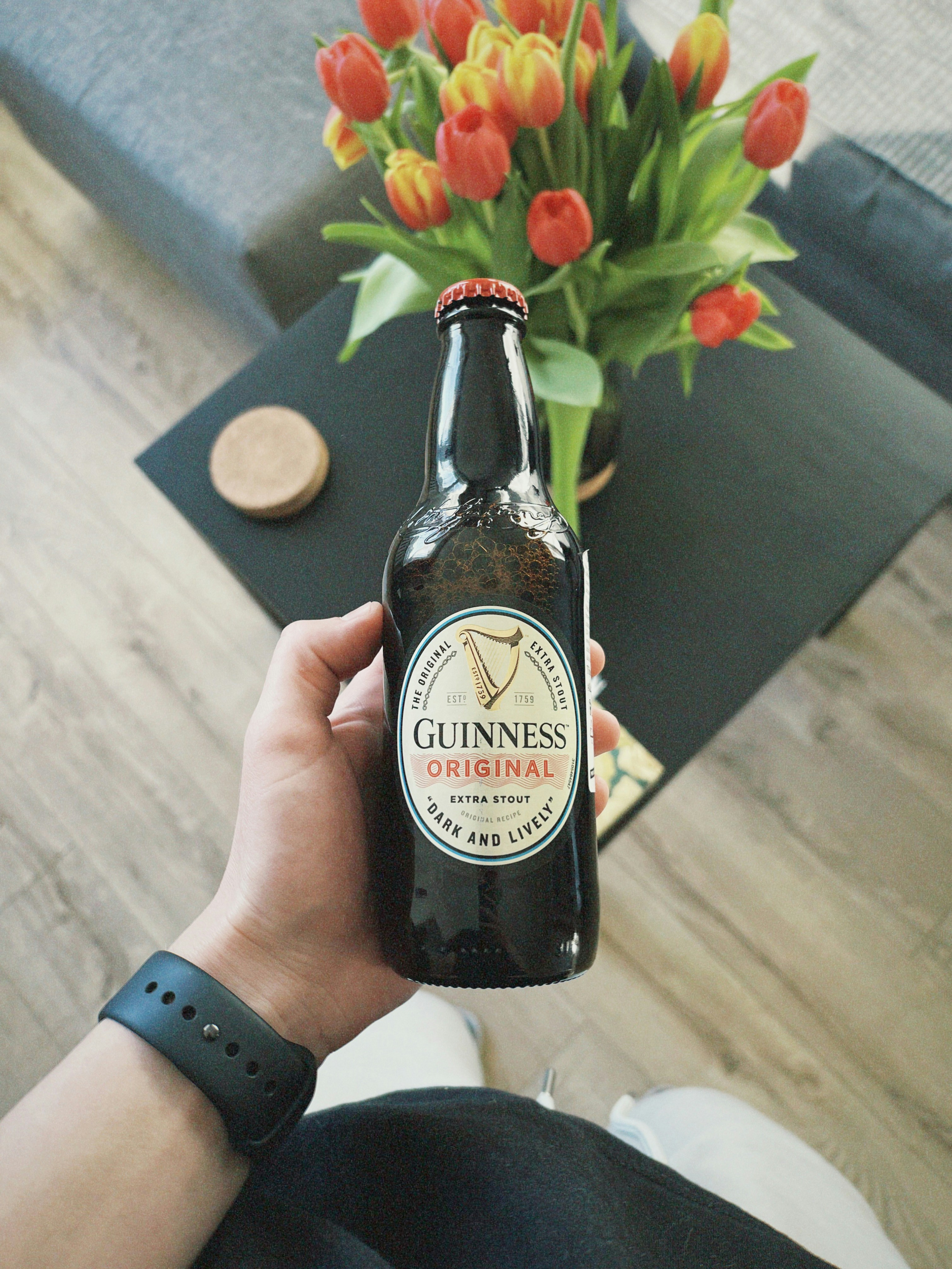 a person holding a bottle of guinness next to a vase of tulips