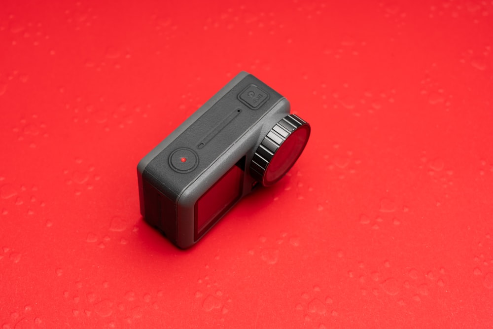 a black camera with a red lens on a red surface