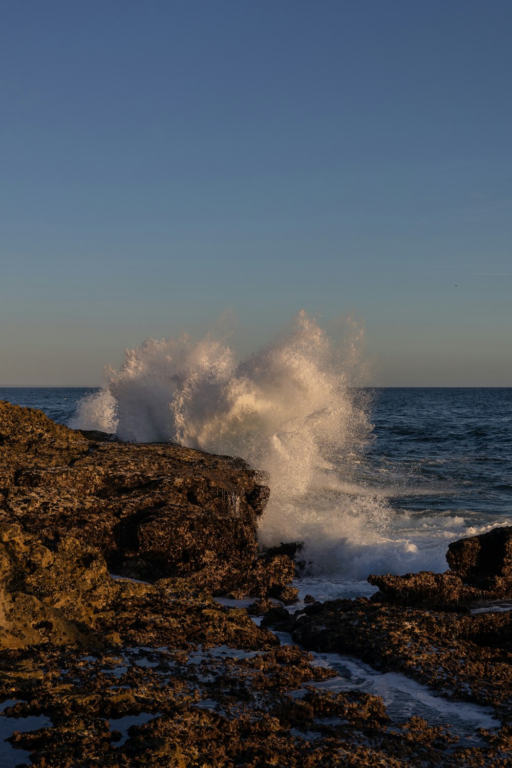 a wave crashing on a rocky shore at sunset