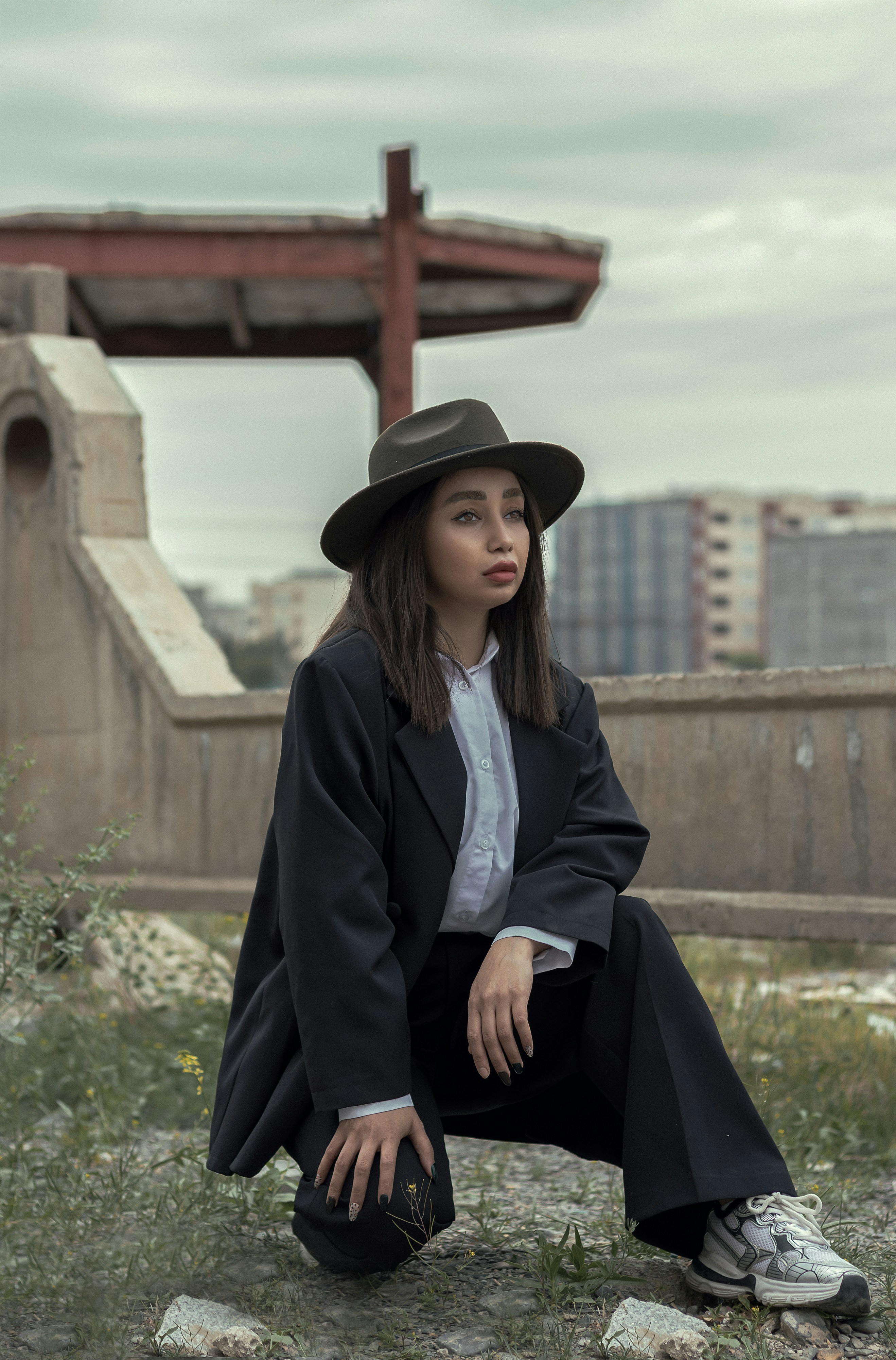 a woman in a black coat and hat sitting on the ground