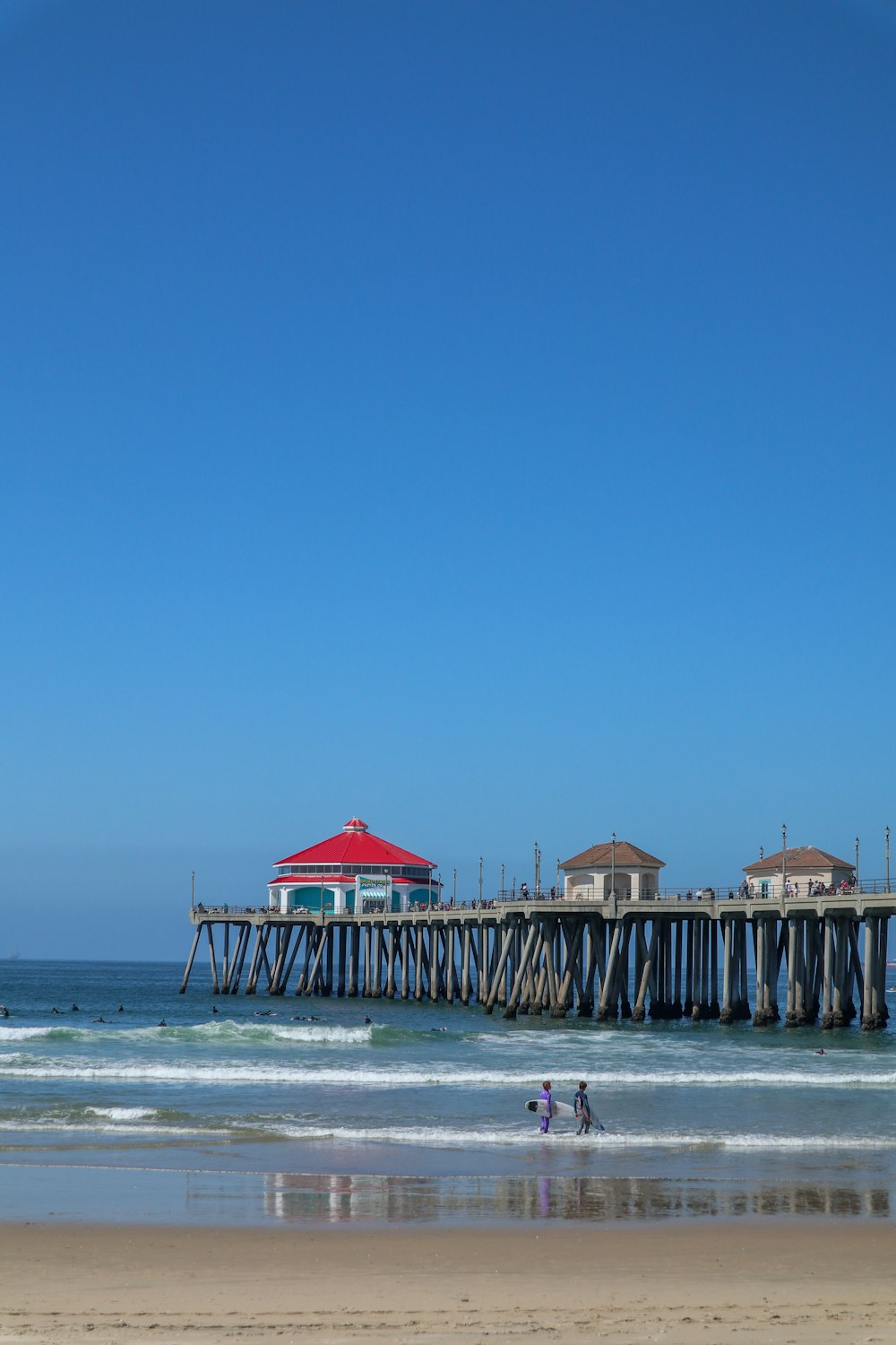 two people walking on the beach near a pier