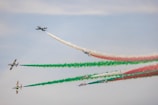 a group of airplanes flying in formation with colored smoke behind them