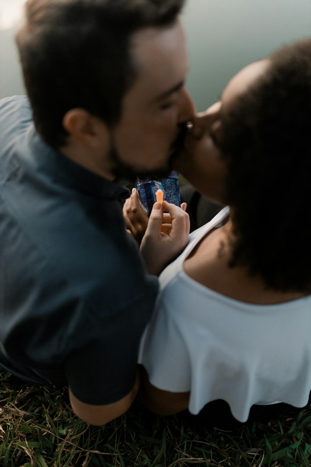 a man and a woman sitting on the grass kissing