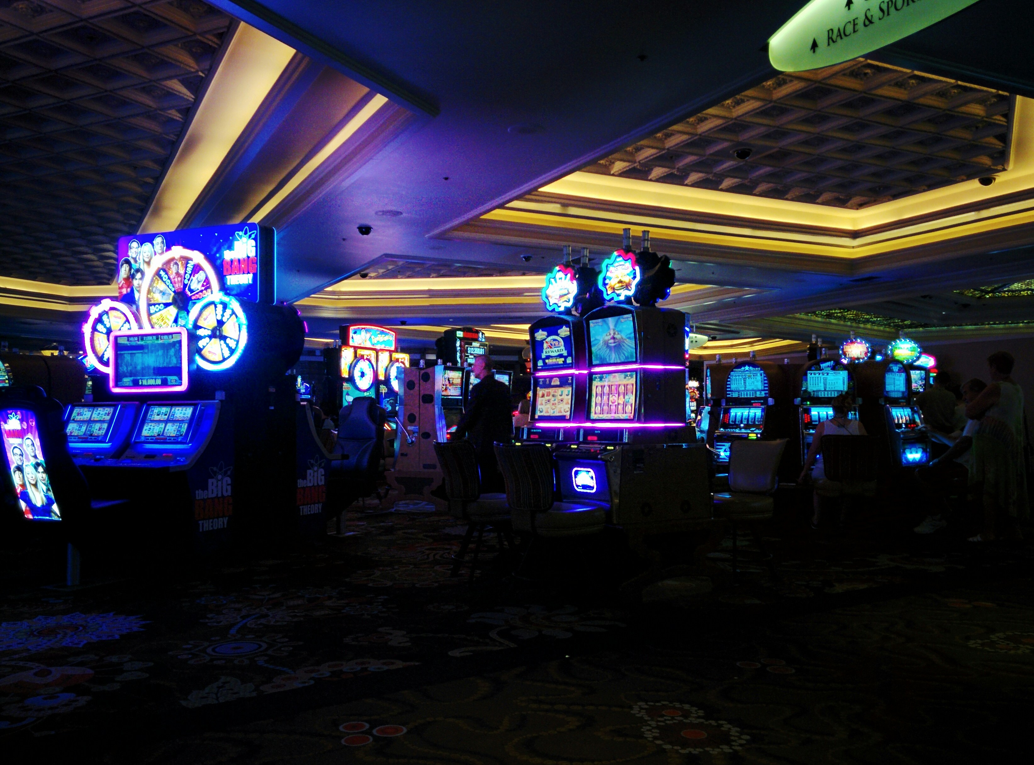 Casino gaming floor with dark lighting, dramatic illuminated slot machines and gaming tables in a premium atmosphere