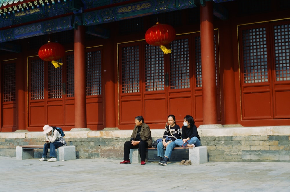 three people sitting on a bench in front of a building