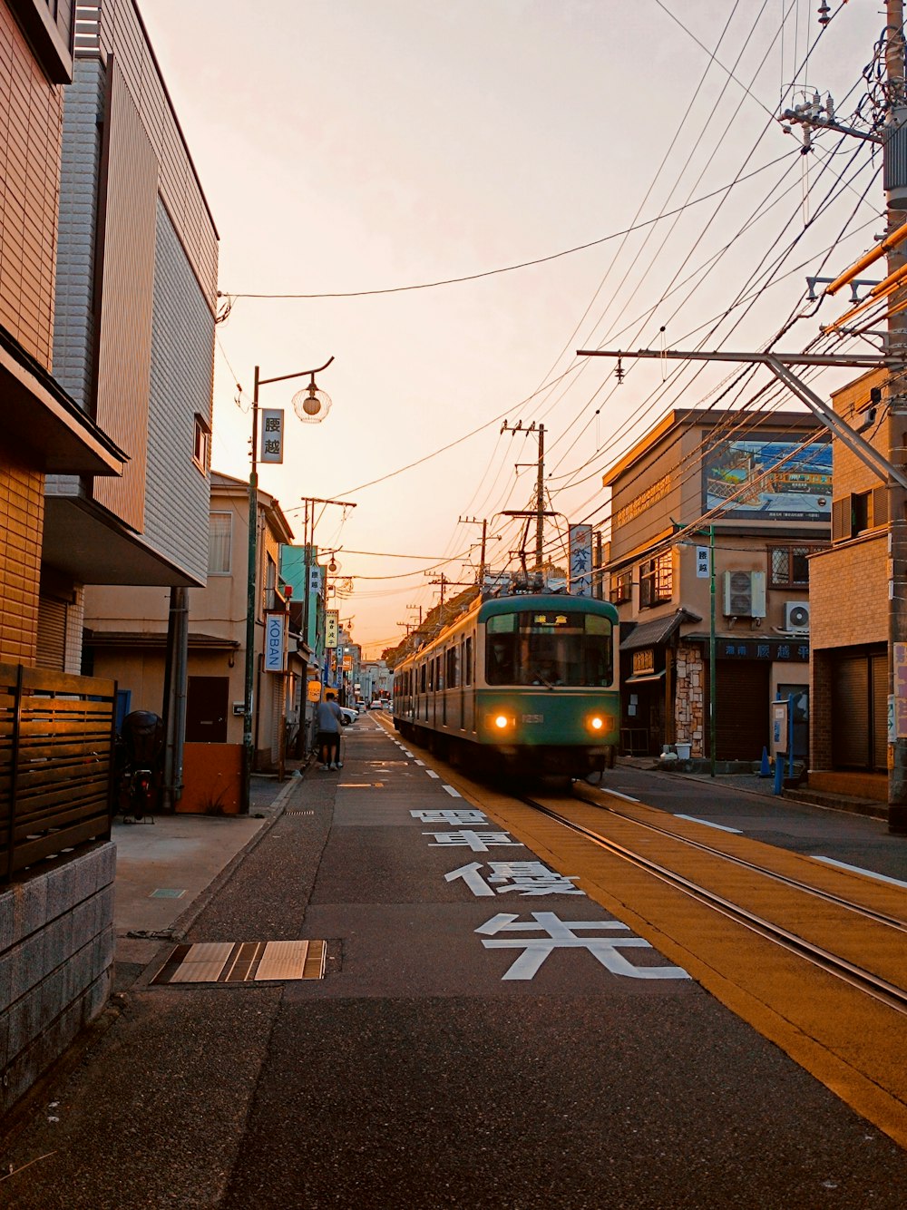 a green train traveling down train tracks next to tall buildings