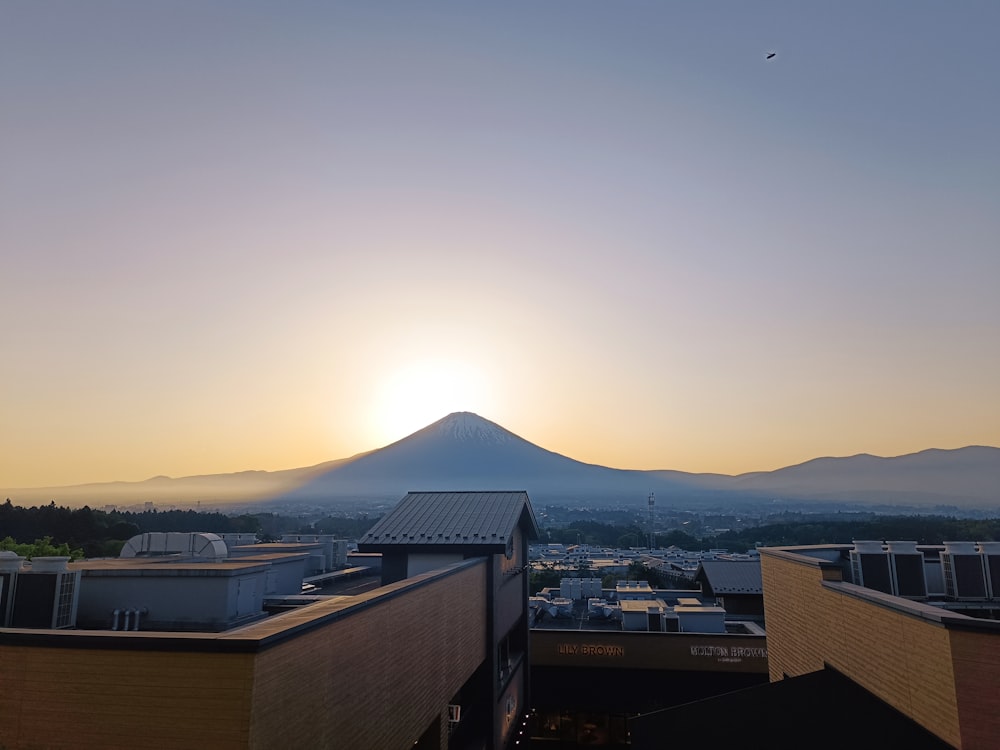 the sun is setting over a city with a mountain in the background