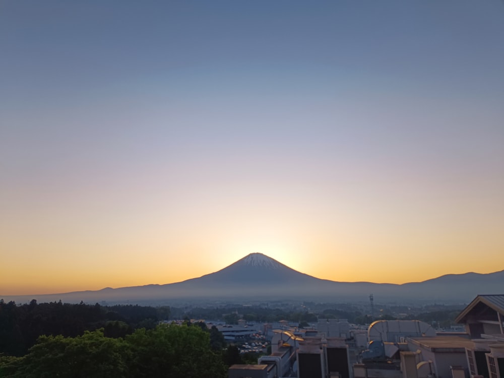 the sun is setting over a city with a mountain in the background