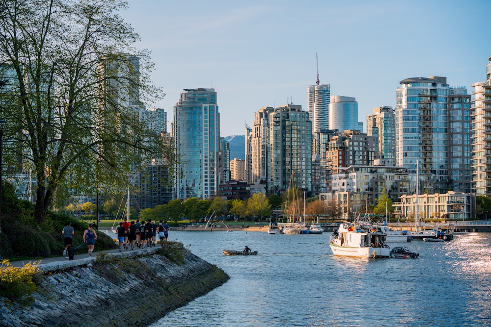 a group of people walking along a river next to tall buildings