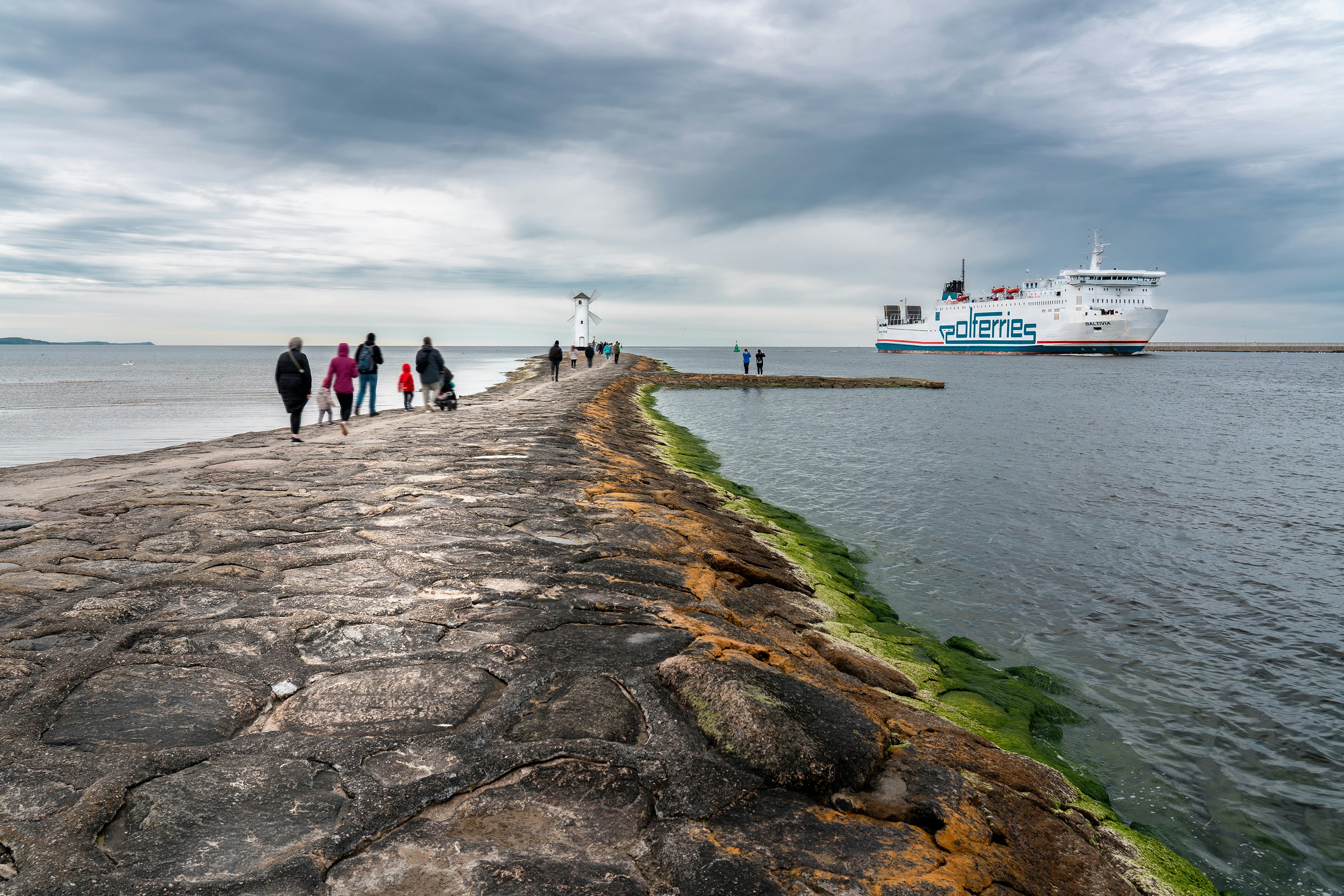 a group of people walking along a pier next to the ocean