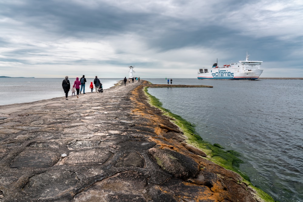 a group of people walking along a pier next to the ocean