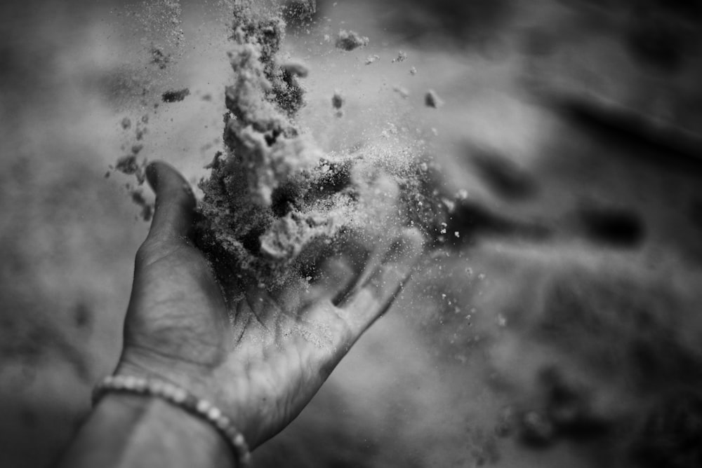 a black and white photo of a hand throwing sand into the air