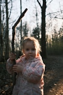 a little girl holding a stick in a forest