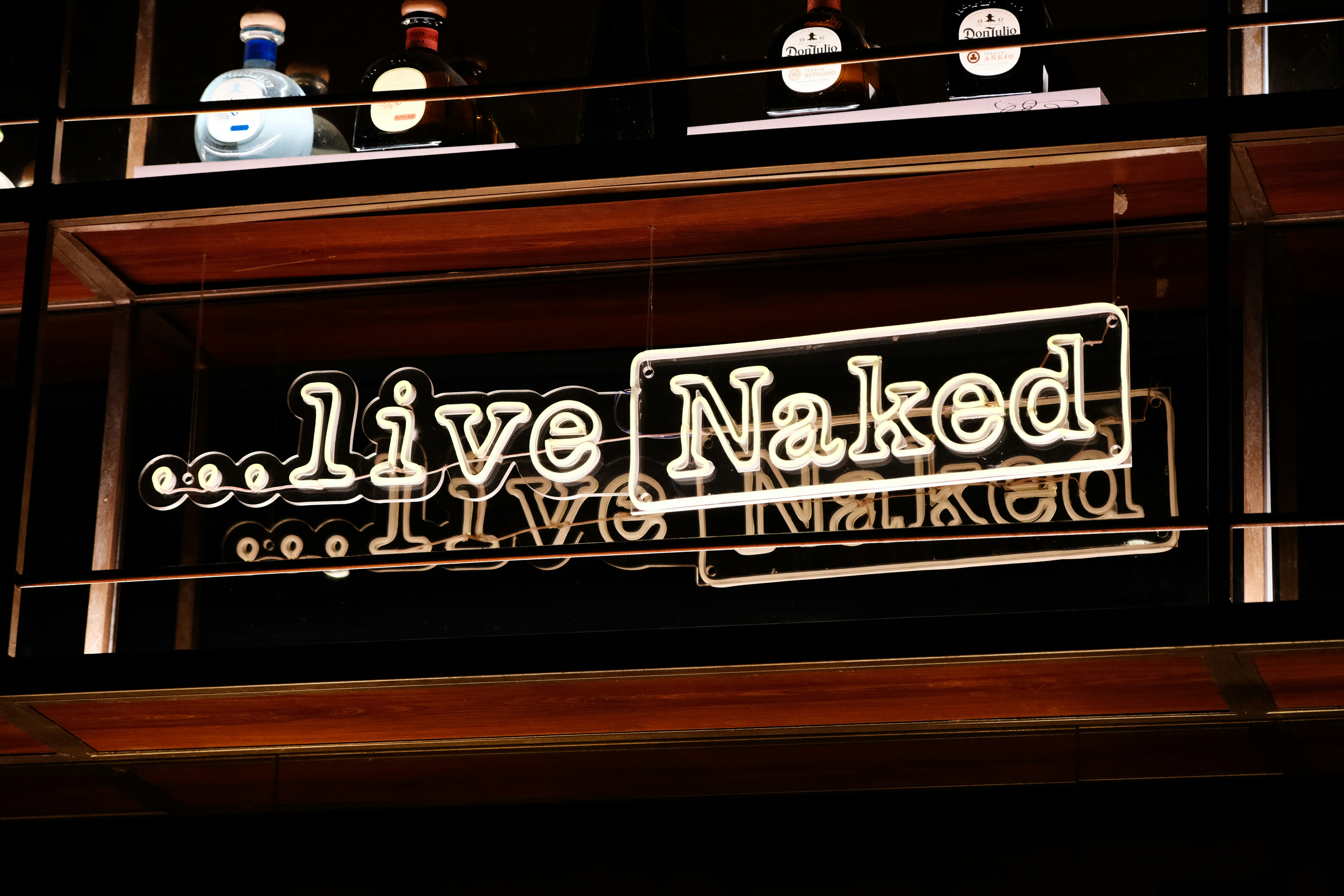 a neon sign that says live naked next to bottles