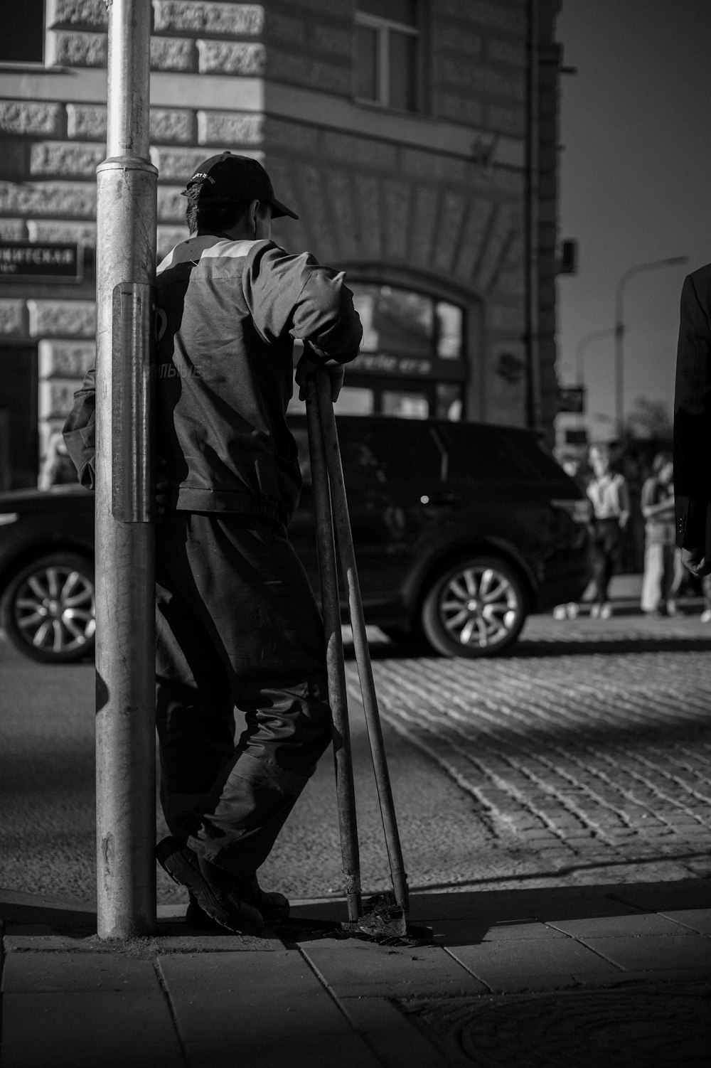 a black and white photo of a man leaning against a pole