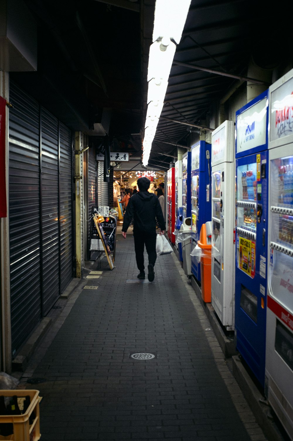 a man walking down a long hallway between vending machines