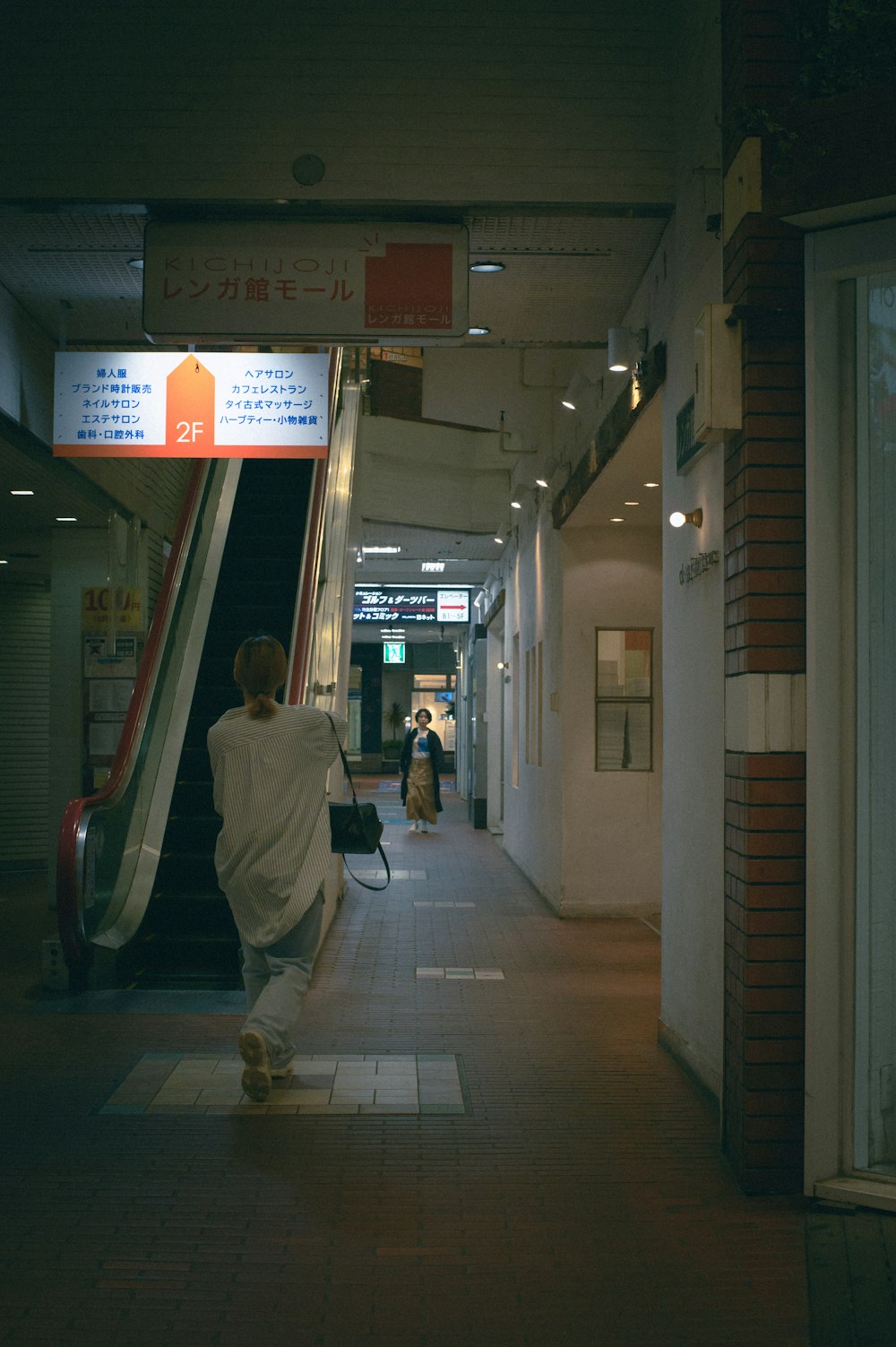 a man walking down a hallway next to an escalator