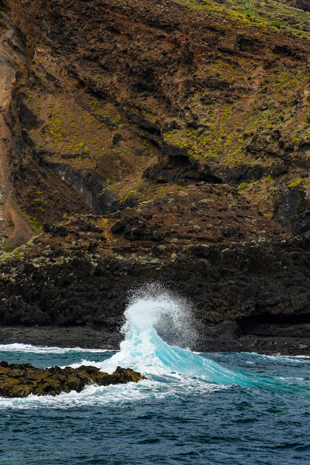 a wave crashing into the ocean near a rocky cliff