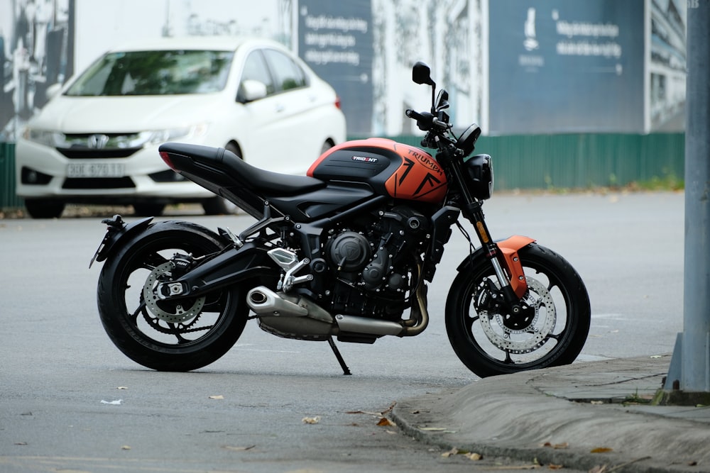 a black and orange motorcycle parked next to a white car