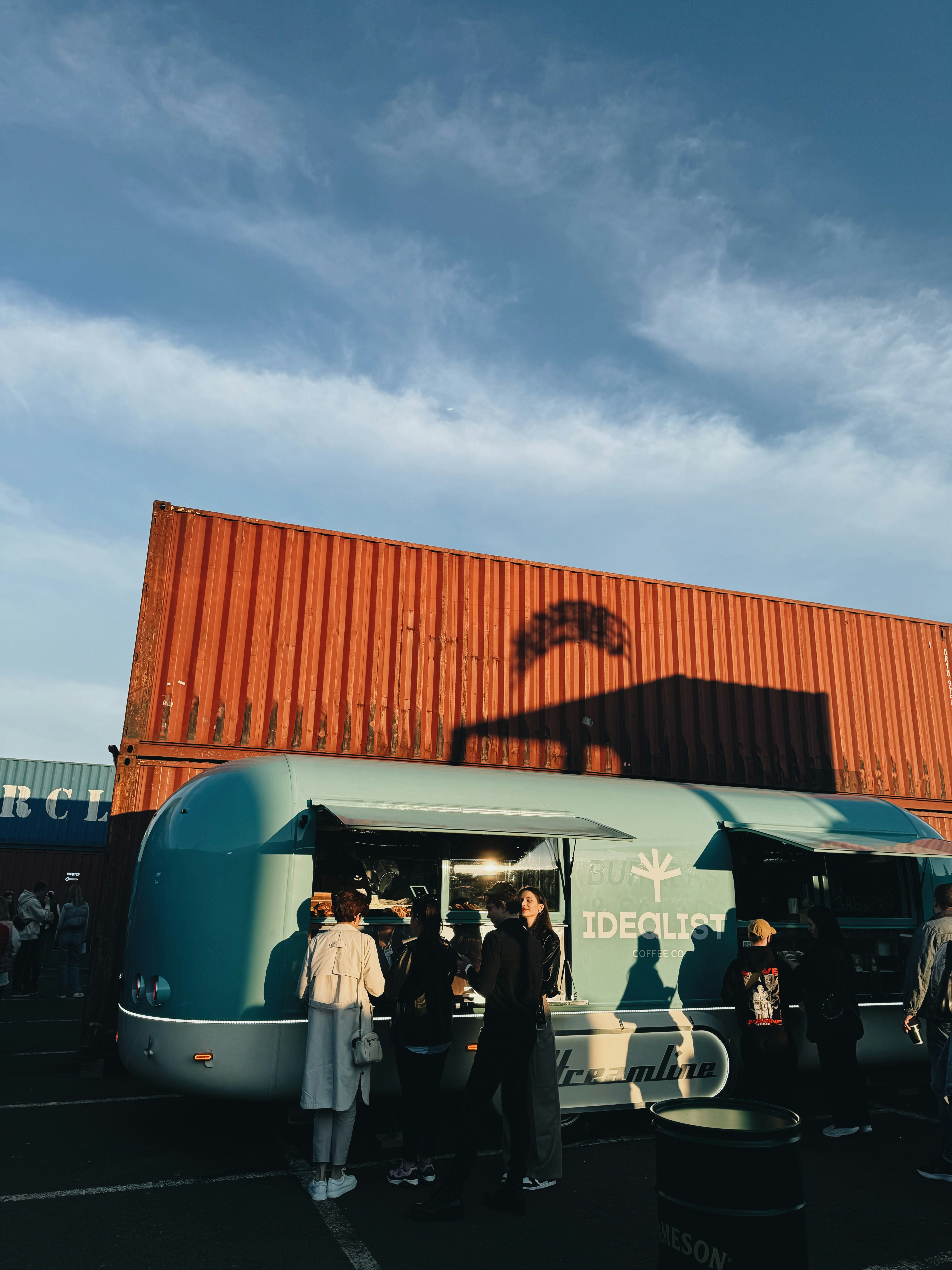 People socialize near a blue food truck with orange containers.