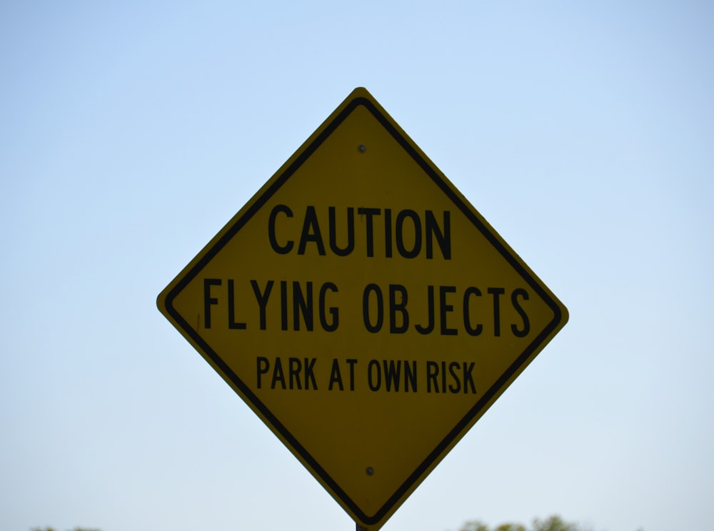 a yellow caution flying objects sign on a pole