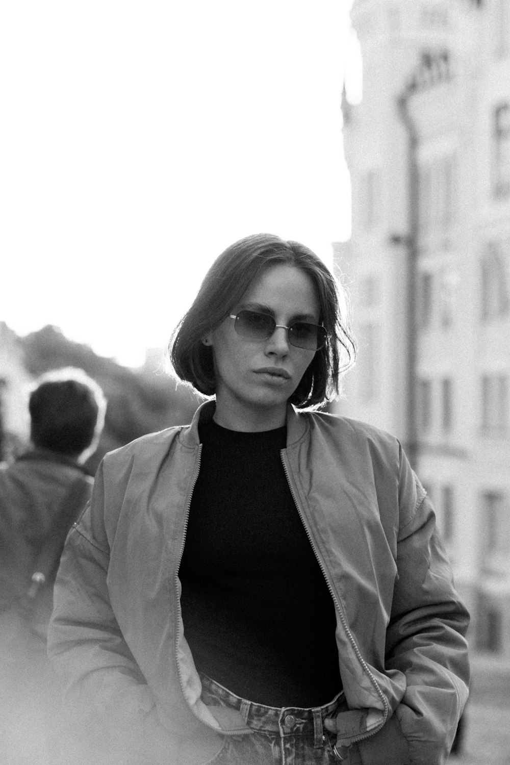 a woman in a jacket and sunglasses walking down a street