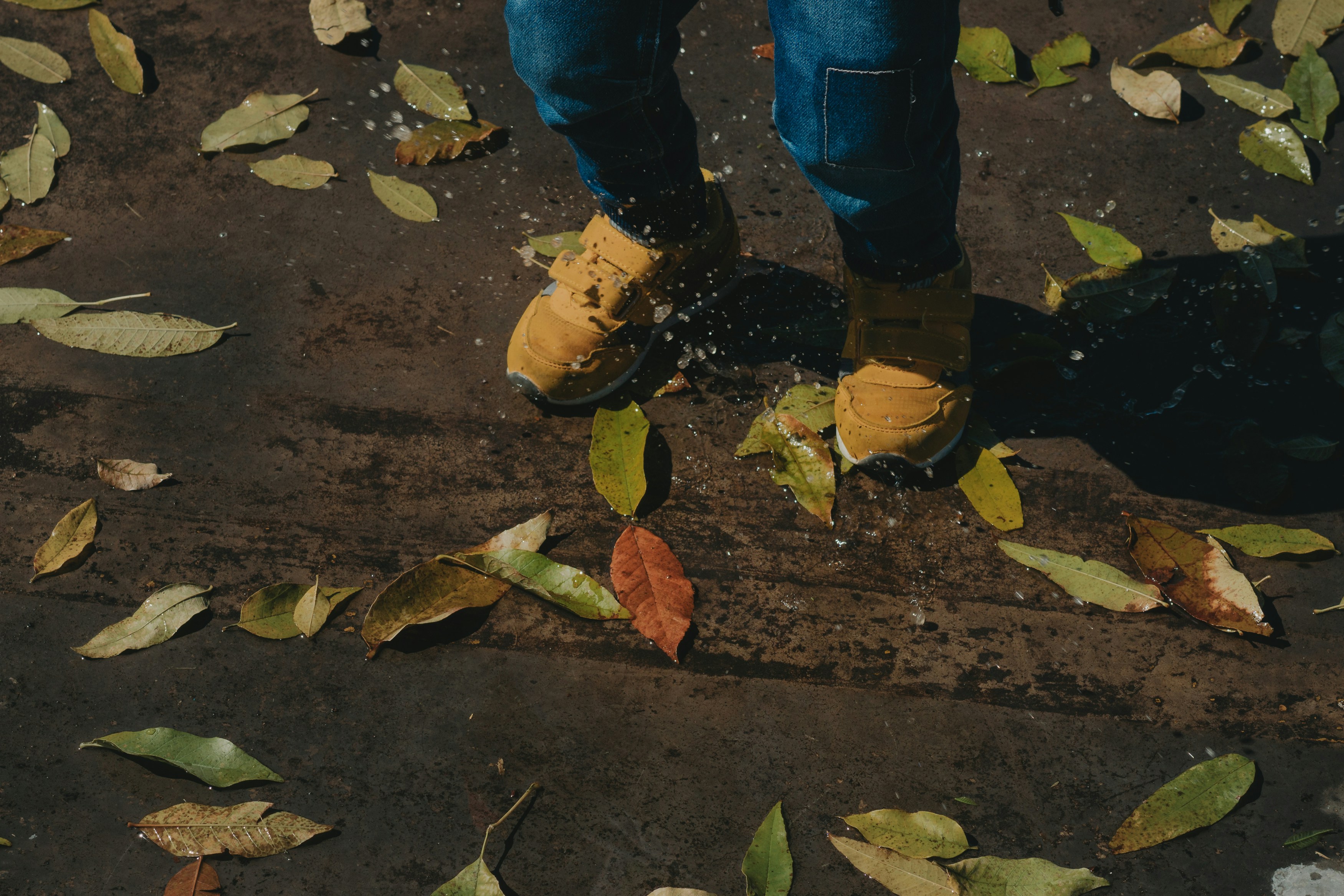 Children in wellies kicking through autumn leaves in a British park on an overcast October day