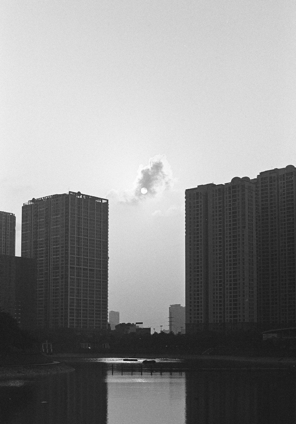 a black and white photo of a body of water with tall buildings in the background