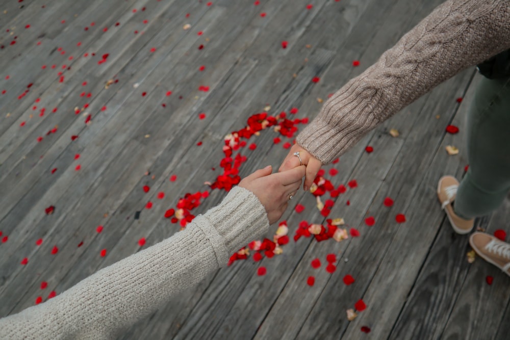 two people holding hands over petals on a wooden floor