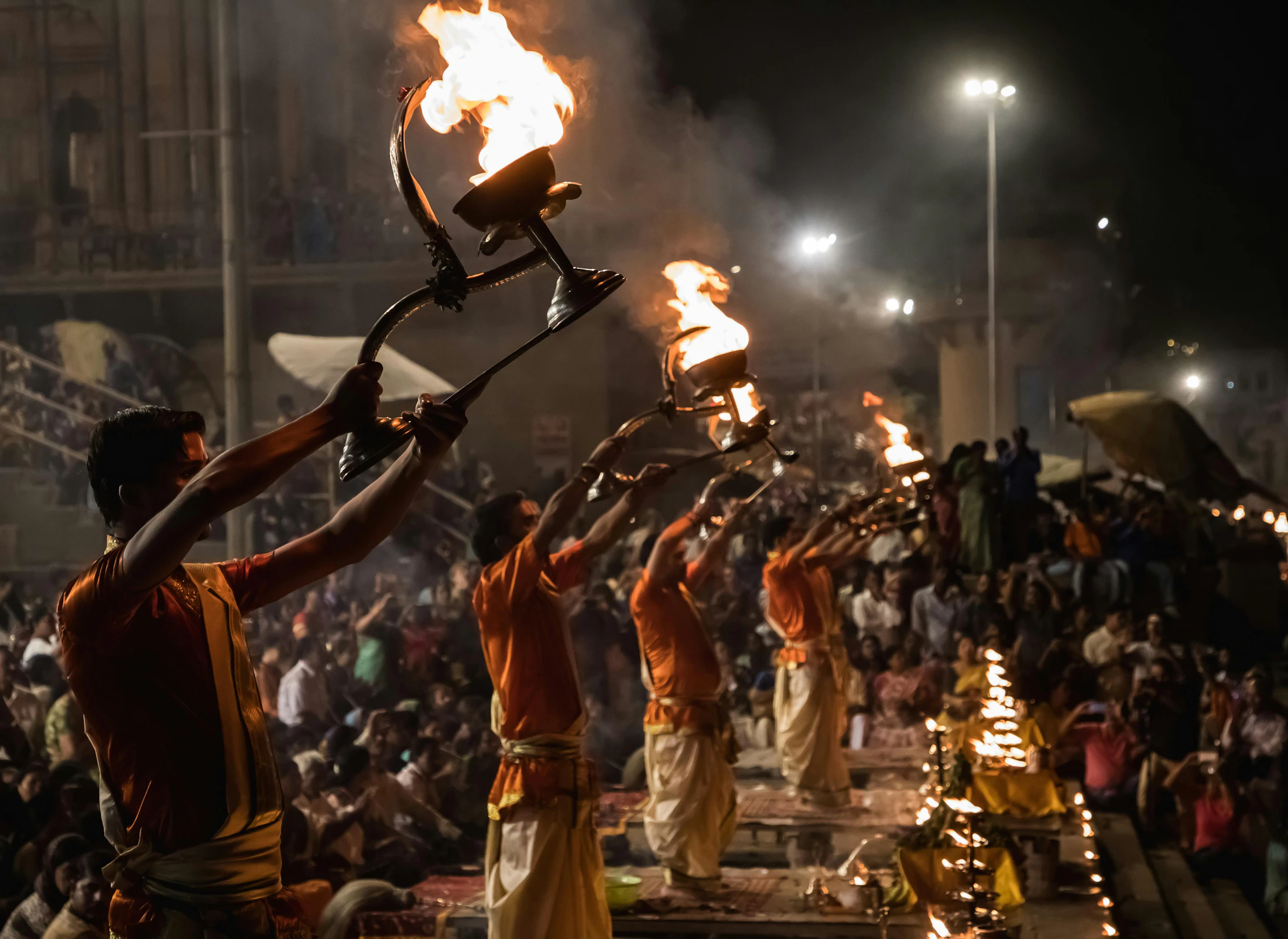 Young priests lifting fire lamps in unison on a Varanasi ghat at night