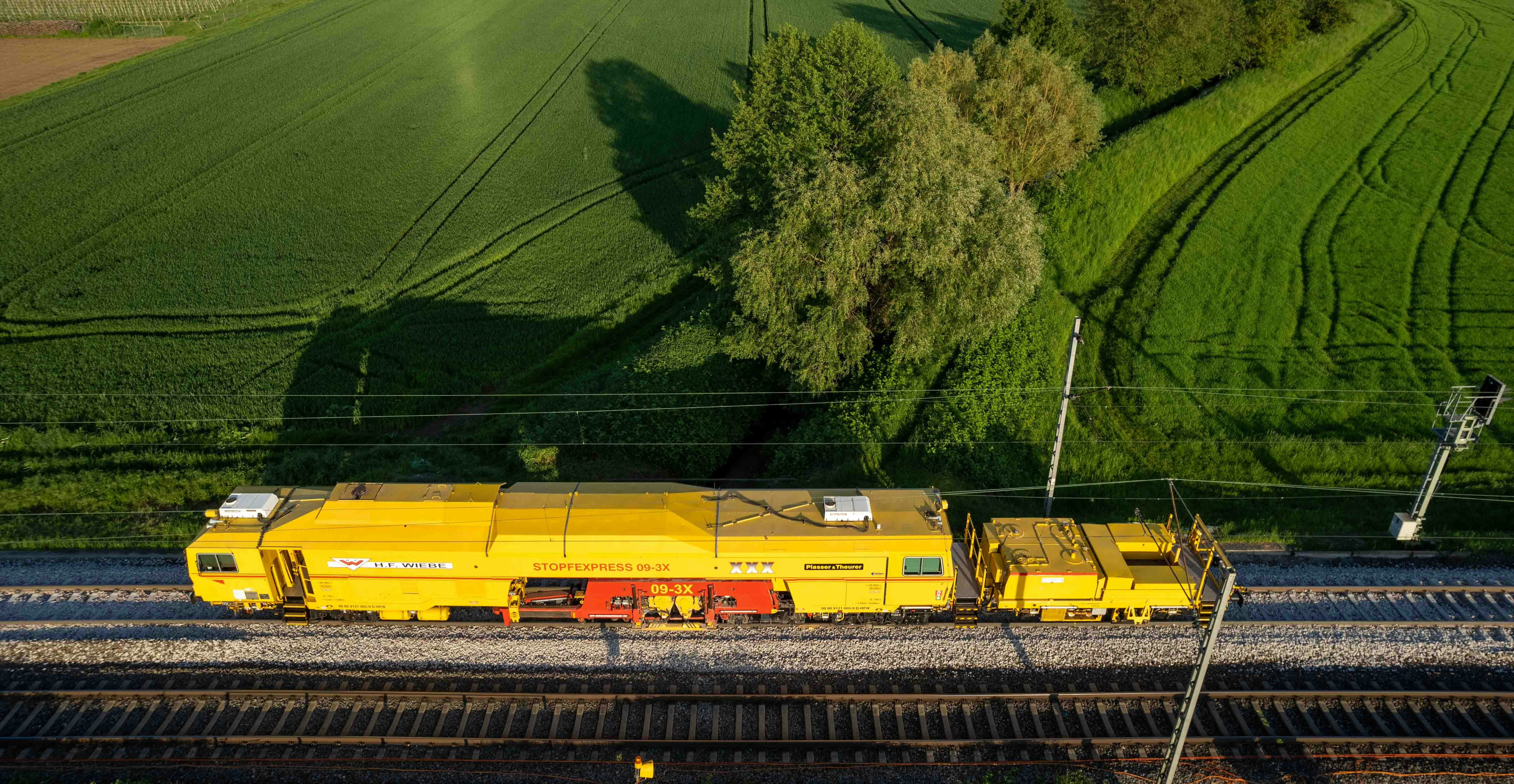 a yellow train traveling down train tracks next to a lush green field