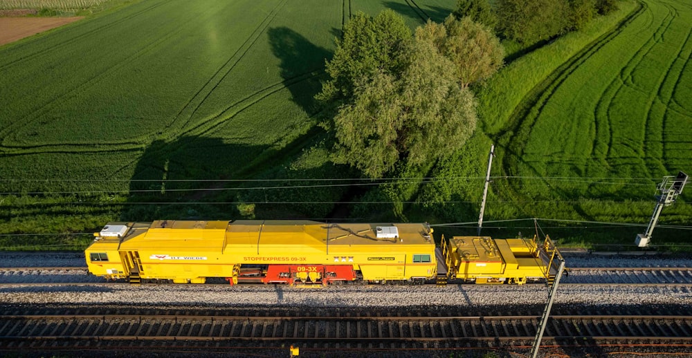 a yellow train traveling down train tracks next to a lush green field