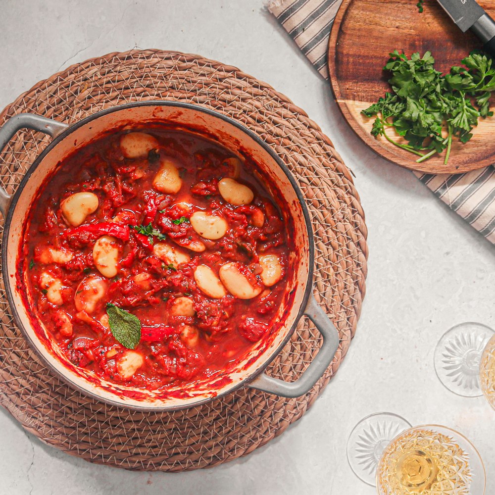 a pot filled with red sauce and garnished with herbs